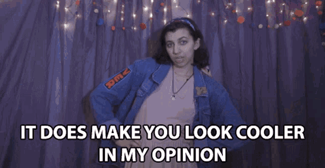 a woman in a denim jacket stands in front of a purple curtain and says it does make you look cooler