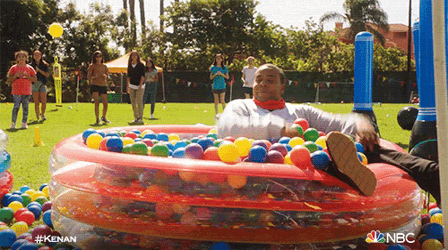 a man is laying in a pool of colorful balls with nbc written on the bottom