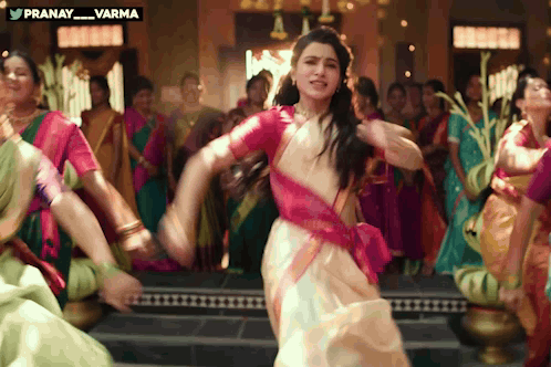 A woman in a sari dances with a group in a festive musical scene.