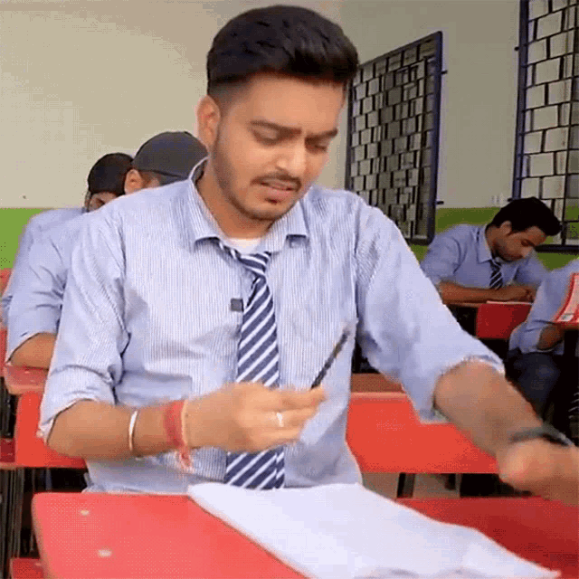 a man in a tie is sitting at a desk in a classroom with other students
