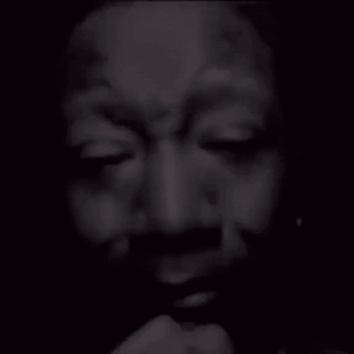 A dark close-up of a person with eyes shut in a solemn expression.