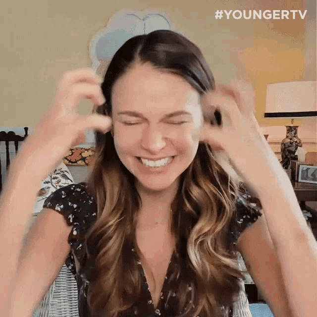 A woman squeezes her eyes shut while pulling at her hair in frustration.