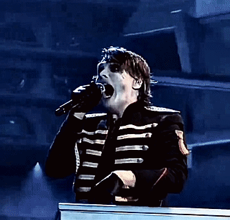 a man in a black jacket is standing in front of a piano and holding a microphone in his hand .