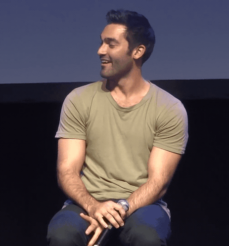 A seated man smiles and turns to the side in a dark studio setting.