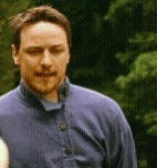a man in a blue shirt is standing in front of a forest .