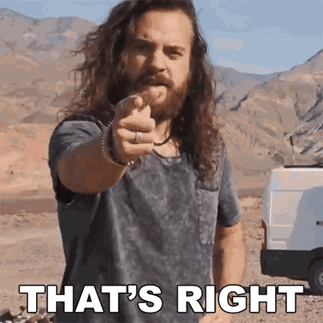 a man with long hair and a beard pointing at the camera with the words that 's right behind him