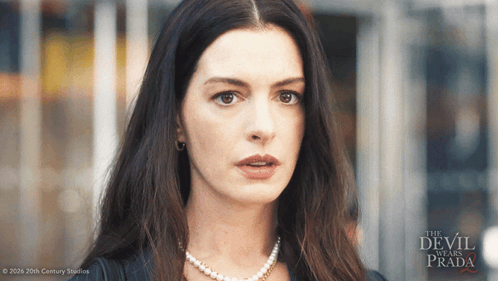 a woman wearing a pearl necklace stands in front of a poster for the movie the devil wears prada