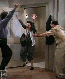 People dance together in a room with their arms raised.