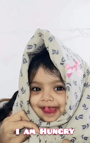 A smiling child under a blanket says “I AM HUNGRY.”