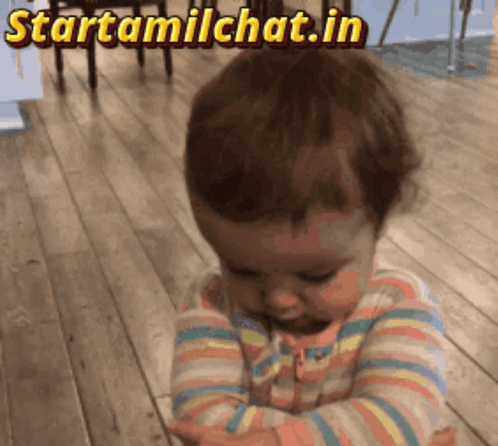 A toddler looks downward sadly while standing indoors.
