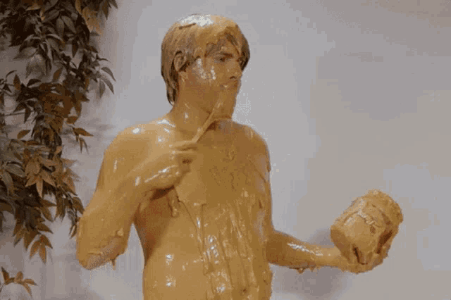 a naked man is covered in peanut butter and holding a bucket