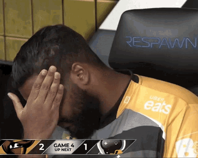Esports player covers his face while seated at a tournament desk.