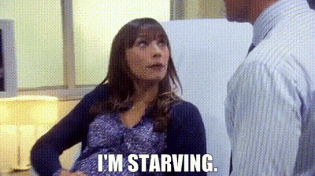 a man and a pregnant woman are standing next to each other and the woman is saying `` i 'm starving '' .