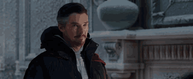 doctor strange is wearing a black jacket and a red cape while standing in front of a fireplace in a room .