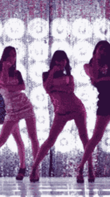 three women are dancing on a stage in front of a wall with purple lights