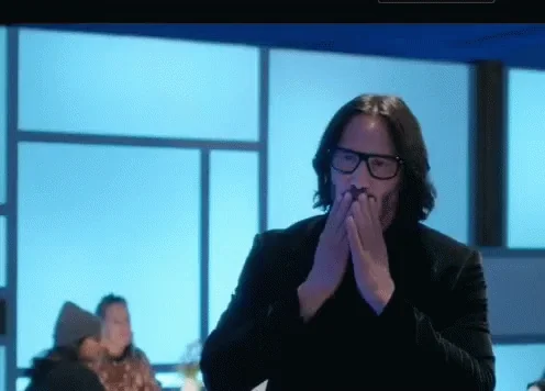 Keanu Reeves covers his mouth in a grateful, emotional gesture.
