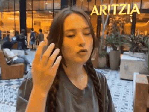 A woman raises her hand in a retail store while the Aritzia sign is behind her.