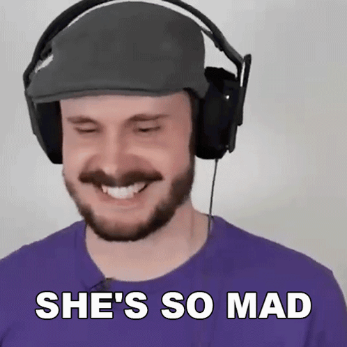 a man with a beard wearing headphones and a hat is smiling and saying she 's so mad .