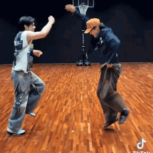 two men are dancing on a wooden floor in front of a basketball net .