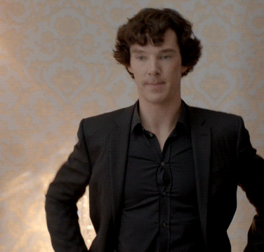 a man in a black suit and black shirt stands with his hands on his hips