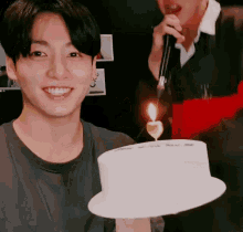 a young man is holding a birthday cake with a candle on it .