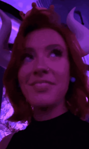 A red-haired costumed woman gives a coy upward glance under purple lighting.