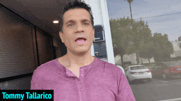 a man in a purple shirt is standing in front of a door with the name tommy tallarico above him