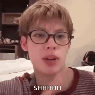 a young man wearing glasses and a striped shirt is making a shhh gesture .