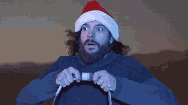 a bearded man wearing a santa hat is holding a hose