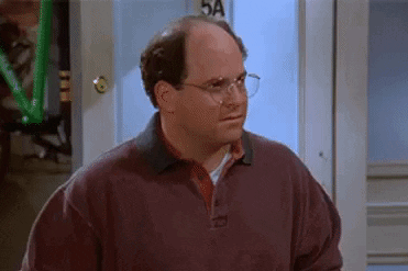 George Costanza looks aside with a dismissive expression in an apartment.
