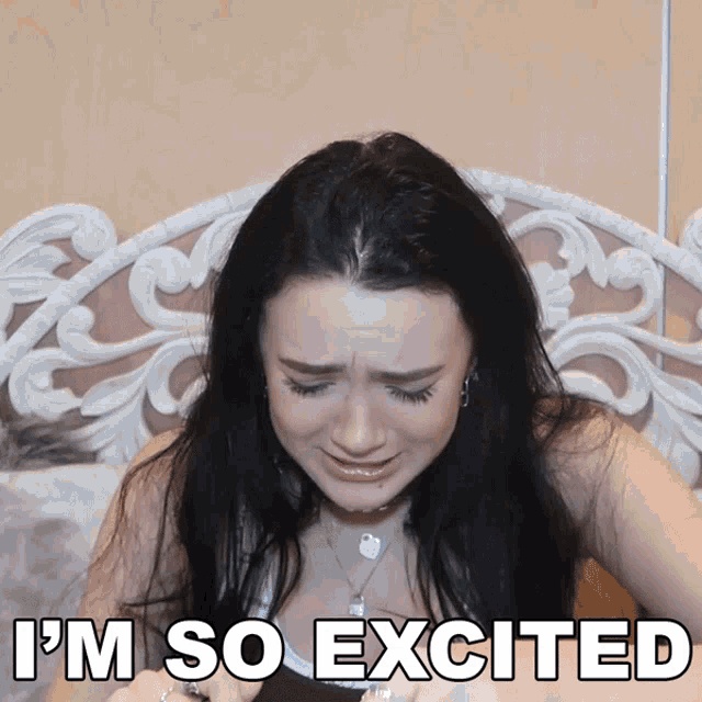 a woman is sitting on a bed with the words i 'm so excited behind her