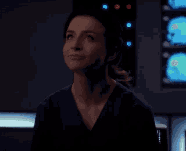 a woman in a scrub top is looking up in a dark room in front of a computer screen .