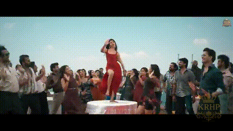 a woman in a red dress is standing on a table in front of a crowd .