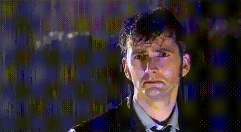 The Tenth Doctor stands in the rain with a devastated expression.