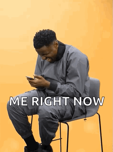 A seated man looks at his phone with the caption “ME RIGHT NOW.”