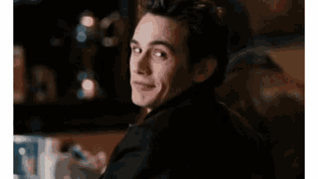 A man looks back over his shoulder and smiles warmly in a dim restaurant.