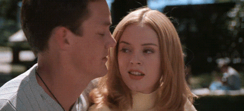 a man and a woman are kissing in a park . the woman is wearing a yellow turtleneck .