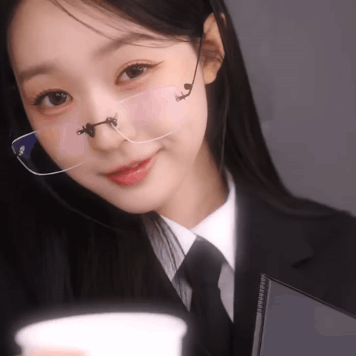 a woman wearing glasses and a suit holds a cup
