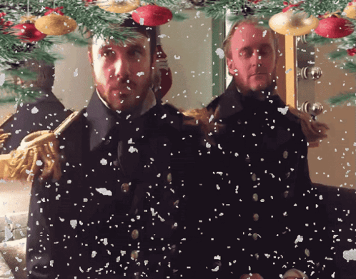 two men are standing in front of a christmas tree with snow falling