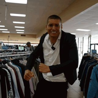 a man in a suit stands in front of a rack of men 's fashions clothes