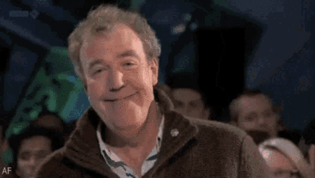 a man is smiling in front of a crowd of people .