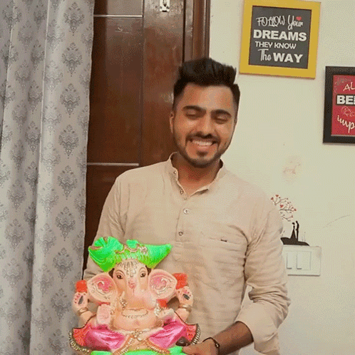 a man holding a statue of ganesha in front of a sign that says " follow your dreams they know the way "