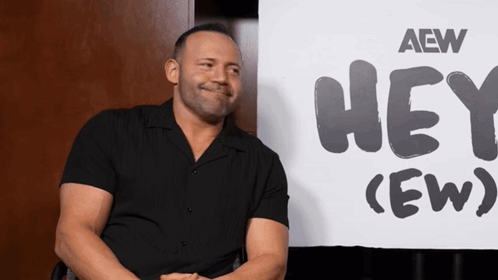 QT Marshall smiles while seated in front of a “HEY! (EW)” backdrop.