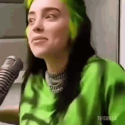 Billie Eilish looks aside at a microphone with green hair roots visible.