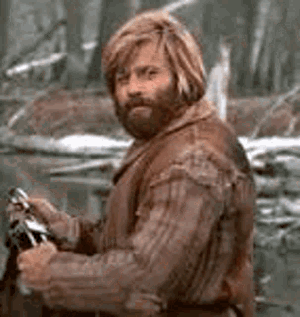 A rugged bearded man outdoors gives a satisfied expression.