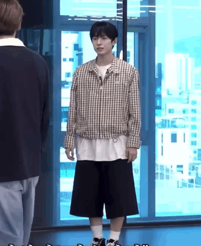a man in a plaid shirt and black shorts is standing in front of a large window .
