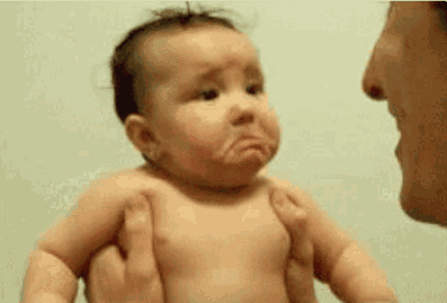 A baby faces an adult with a pouty, tearful expression.