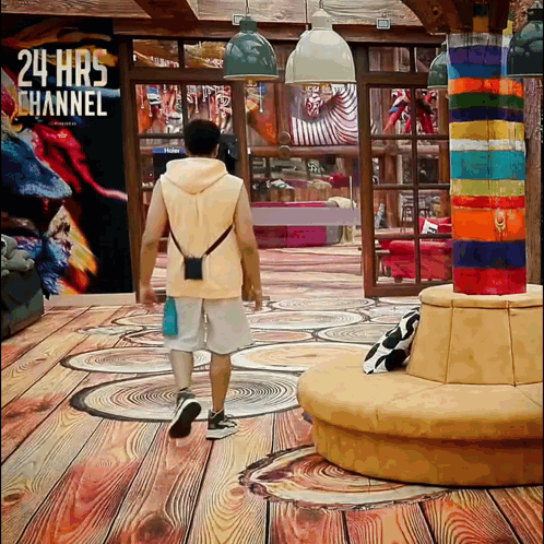a man walking in a room with a 24 hrs channel sign on the wall