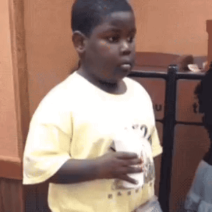 A child stands holding a drink and gives a wary side-eye.