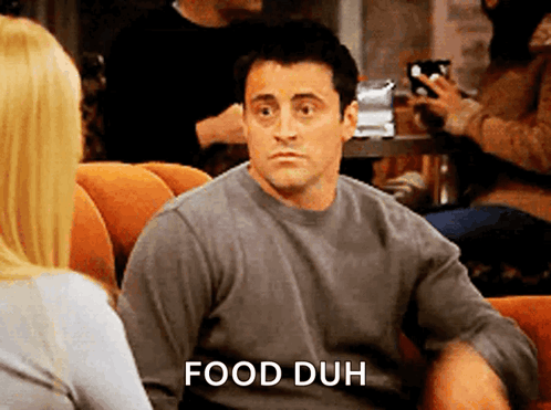 a man in a grey shirt is sitting in a chair with the words food duh behind him